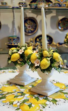 two white vases filled with yellow flowers on top of a table covered in plates