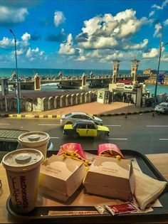 two cups of coffee are sitting on a tray with some food in front of the ocean