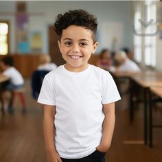 a young boy in a white shirt and black pants smiles at the camera while standing in a classroom