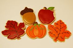 four decorated cookies with leaves, an apple, and a pumpkin on top of each cookie