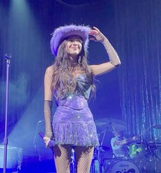 a woman in a purple dress and hat on stage