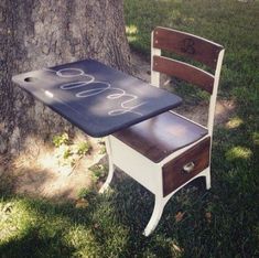 a wooden chair sitting next to a table with writing on it and a tree in the background