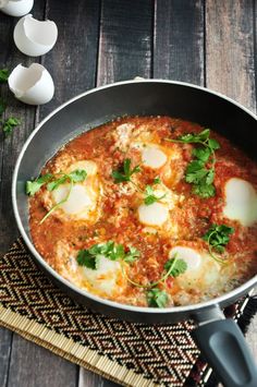 an iron skillet filled with food on top of a wooden table next to eggs and parsley