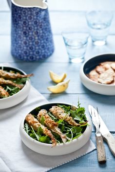 two white bowls filled with food on top of a blue table cloth next to silverware