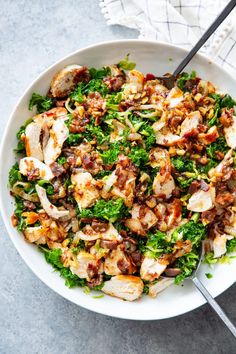 a white bowl filled with chicken and greens on top of a table next to a fork