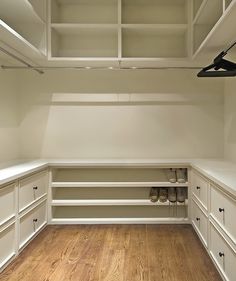 an empty walk in closet with wooden floors and white cabinets, along with wood flooring