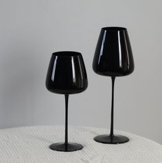 two black wine glasses sitting on top of a white table next to eachother