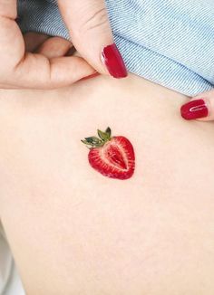 a woman's stomach with a strawberry tattoo on the side of her belly and red nail polish