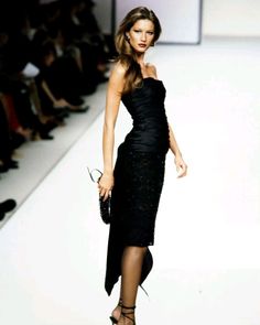 a woman is walking down the runway in a black dress