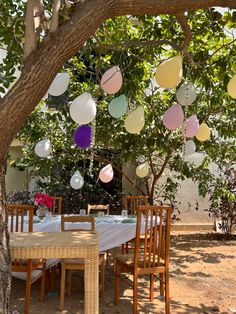 an outdoor dining area with table, chairs and balloons hanging from the trees above it