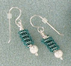 two green and silver earrings sitting on top of a gray table next to a pair of scissors