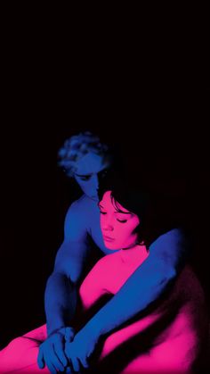 a man and woman sitting next to each other in the dark with neon colors on them