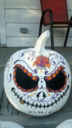 a white pumpkin decorated with black eyes and orange flowers sitting on the ground next to a chair