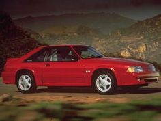 a red sports car parked on the side of a road in front of some mountains