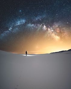 a man standing on top of a snow covered slope under a night sky filled with stars