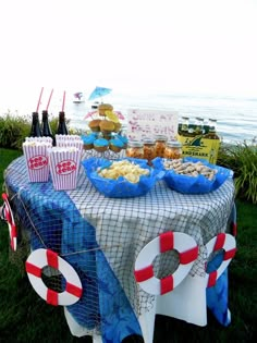 a table that has some food on it and drinks in front of the ocean shore