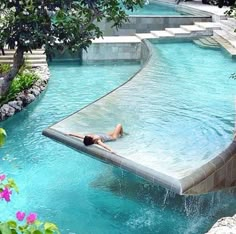 a man is swimming in a pool surrounded by trees and flowers on the other side