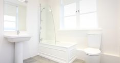 a white bathroom with a sink, toilet and bathtub next to a window on the wall