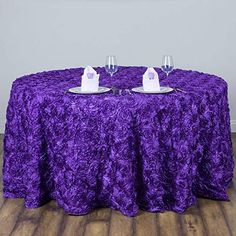 two wine glasses sitting on top of a table covered in purple cloth with white plates