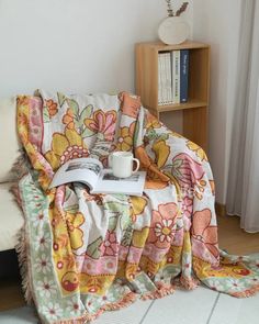 a couch covered in a blanket with a coffee cup on top of it next to a book shelf