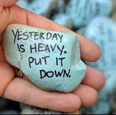 a hand holding a rock with writing on it that says, yesterday is heavy put it down