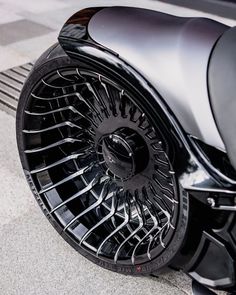 the front wheel and tire of a black motorcycle parked on a tile floor next to a metal grate