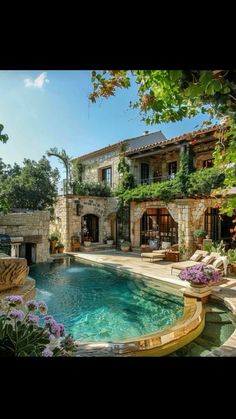 an outdoor swimming pool surrounded by greenery and stone walls, next to a house