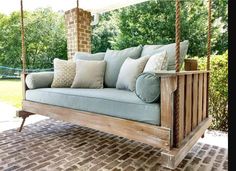 a wooden swing bed with pillows on it in front of a brick wall and trees