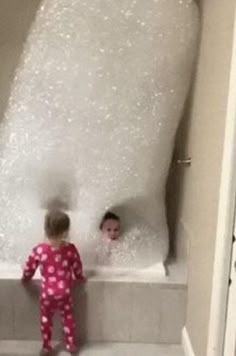 two children are in the bathtub with foam on it and one is wearing pajamas