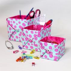 three pink and blue polka dot boxes with scissors, clips, and other items in them