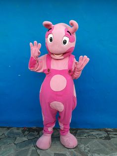 a pink dinosaur mascot standing in front of a blue wall with his hands up to the side