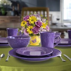 purple and yellow flowers are in a vase on a table set for two with matching dishes