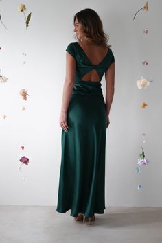 a woman in a long green dress looking back at the wall with flowers on it