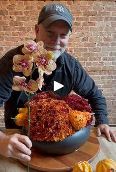 a man sitting at a table with some flowers in front of him and two pumpkins behind him