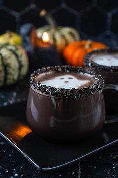 two glasses filled with chocolate pudding sitting on top of a black plate next to mini pumpkins