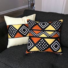 two black and yellow pillows sitting on top of a gray couch next to each other