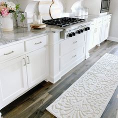 a kitchen with white cabinets and marble counter tops, along with a rug on the floor