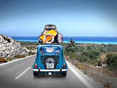 an old vw bus with luggage on top driving down the road by the ocean