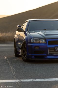 the blue car is parked on the side of the road in front of some hills