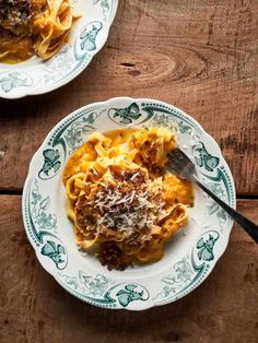 two plates filled with pasta and sauce on top of a wooden table next to a fork