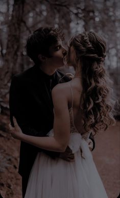 a man and woman are kissing in the woods, one is wearing a wedding dress