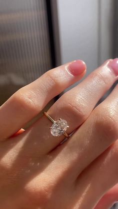 a woman's hand with a diamond ring on top of her finger, in front of a window