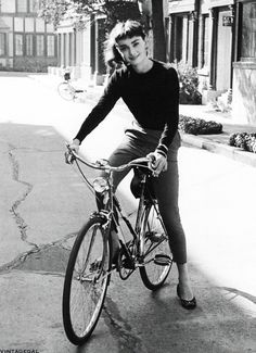 a black and white photo of a woman on a bicycle