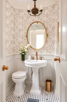 a white toilet sitting next to a sink in a bathroom under a round mirror on the wall