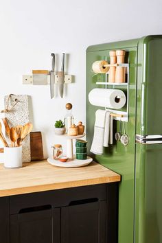 a kitchen with green refrigerator and wooden cutting board on top of it, surrounded by utensils