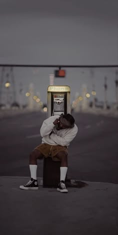 a man sitting on top of a box talking on a cell phone next to a parking meter