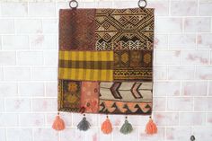 a wall hanging made out of different types of fabric with tassels on it