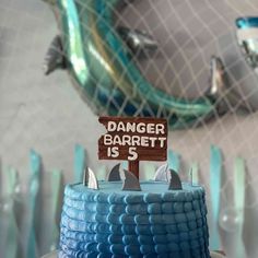 a blue cake with a sign that says danger barrel is s on top and shark fin decorations behind it