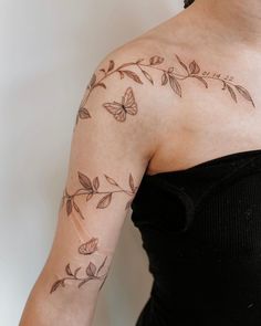 a woman with a butterfly tattoo on her arm and shoulder, standing in front of a white wall