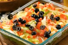 a salad with olives and lettuce in a glass dish on a table